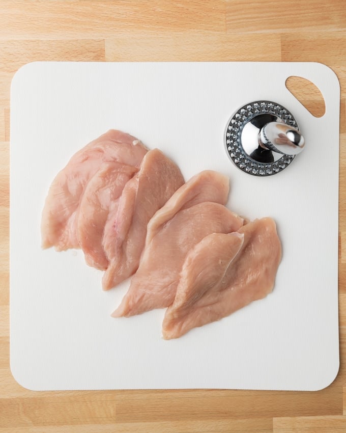 chicken cutlets on a white cutting board with a meat mallet