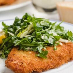 chicken milanese on a white plate with arugula salad
