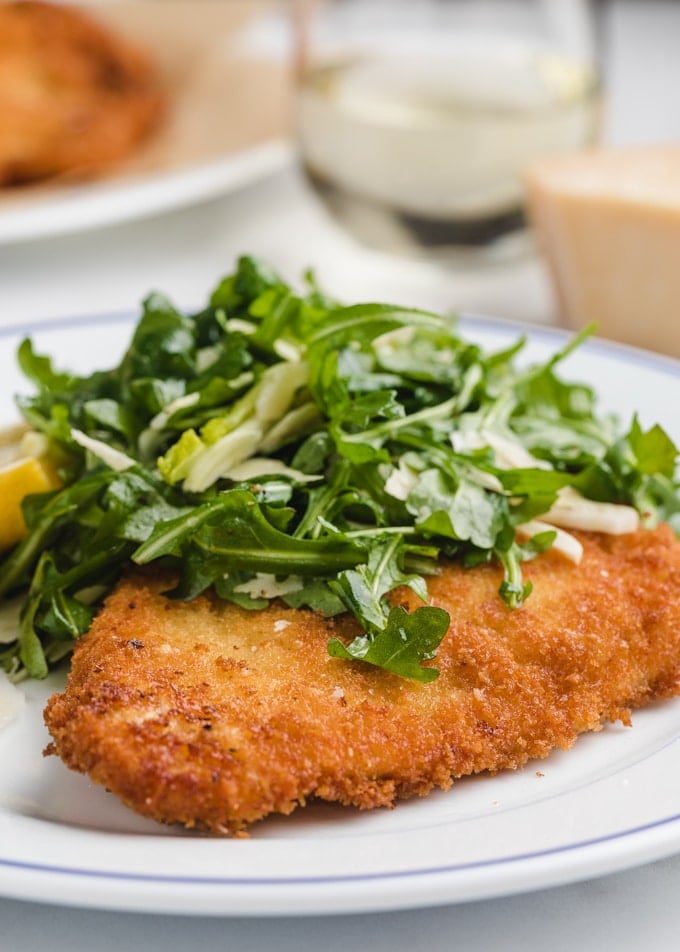 chicken milanese on a white plate with arugula salad