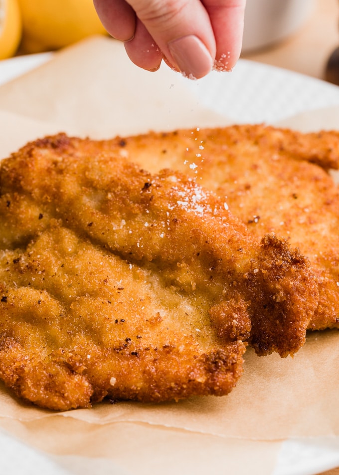 sprinkling salt over freshly-fried chicken milanese