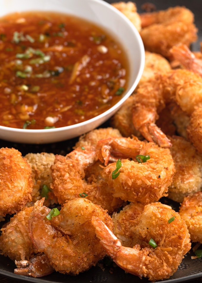 closeup of coconut shrimp on a serving platter with a bowl of orange-chili dipping sauce