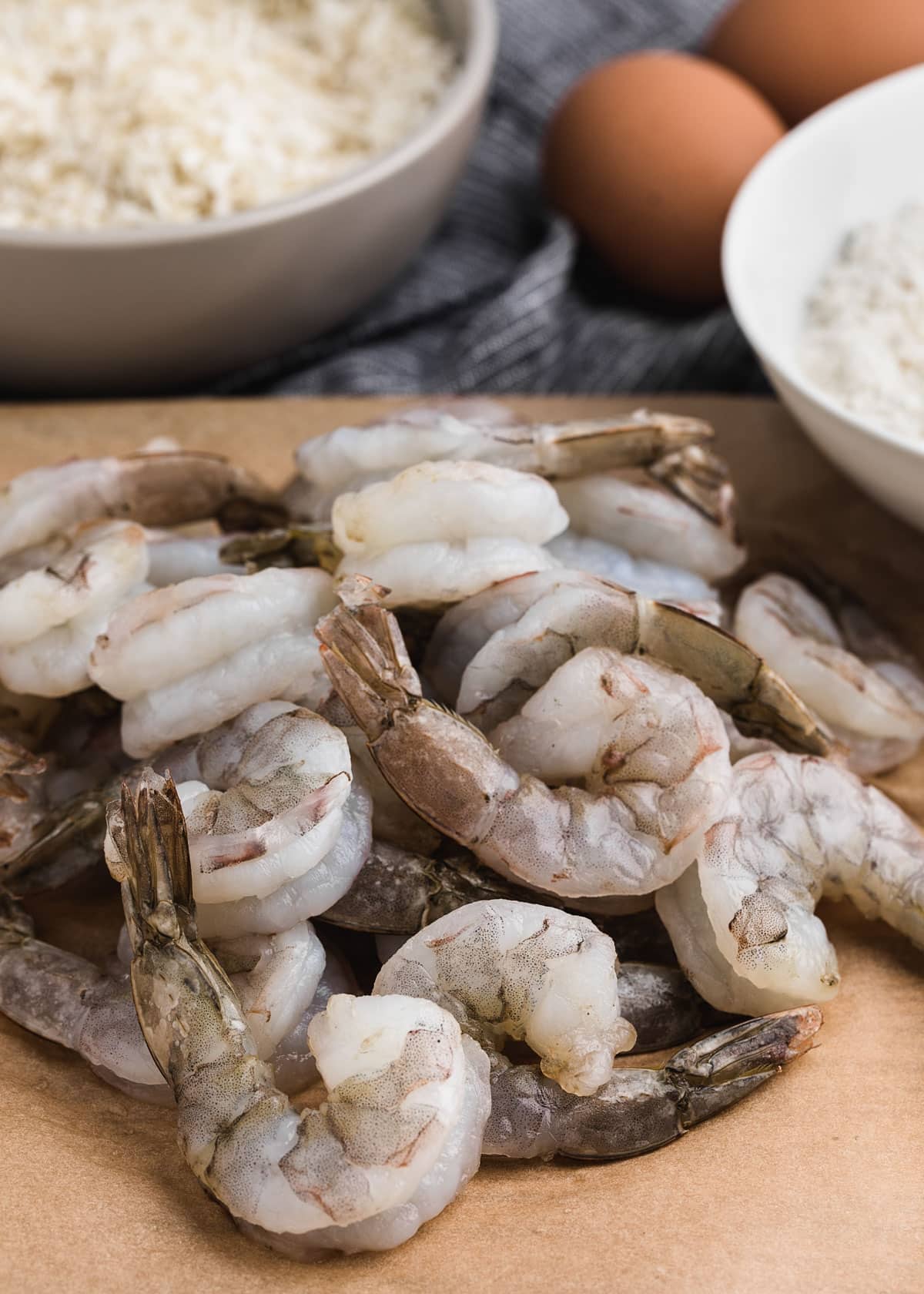 raw shrimp on butcher paper next to bowls of shredded coconut and flour