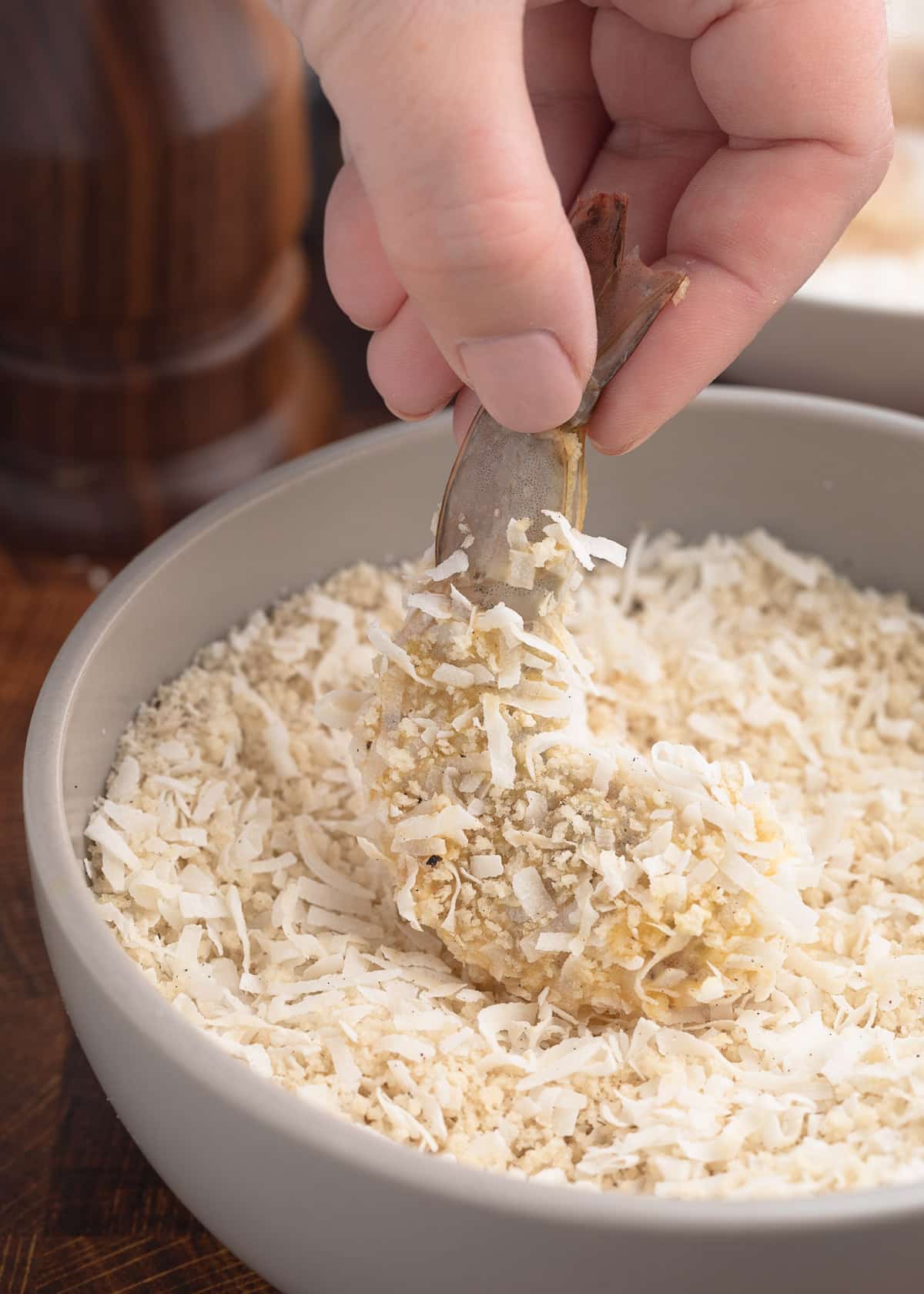 raw shrimp being coated in a panko breadcrumb and shredded coconut mixture in a bowl