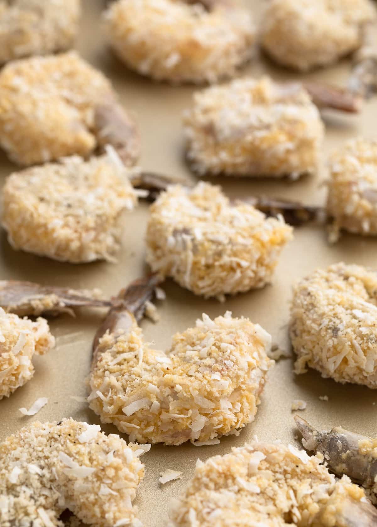 raw breaded coconut shrimp lined up on a baking sheet for baking or frying