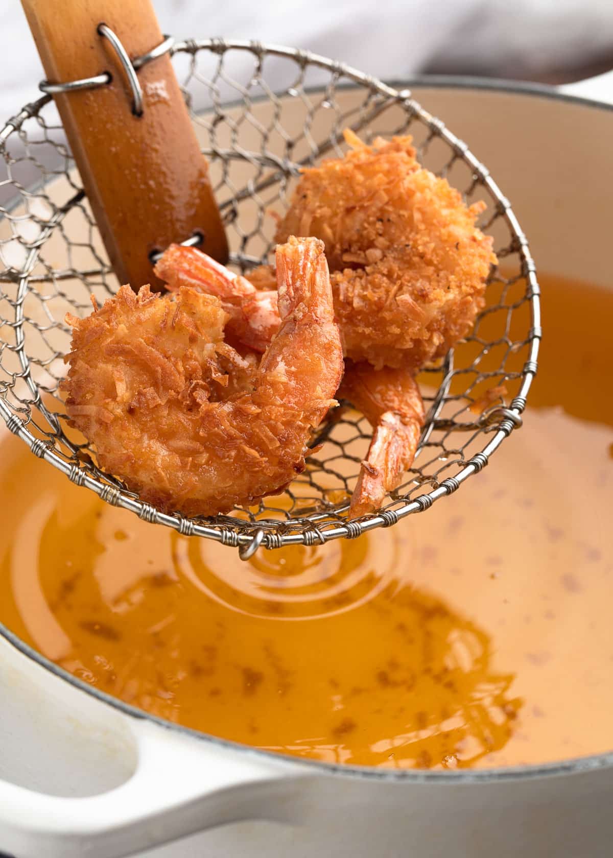 deep fried coconut shrimp on a spider strainer over a pot of deep frying oil