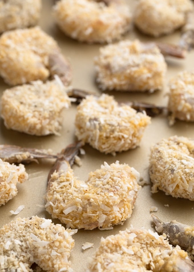 uncooked breaded coconut shrimp on a gold sheet pan