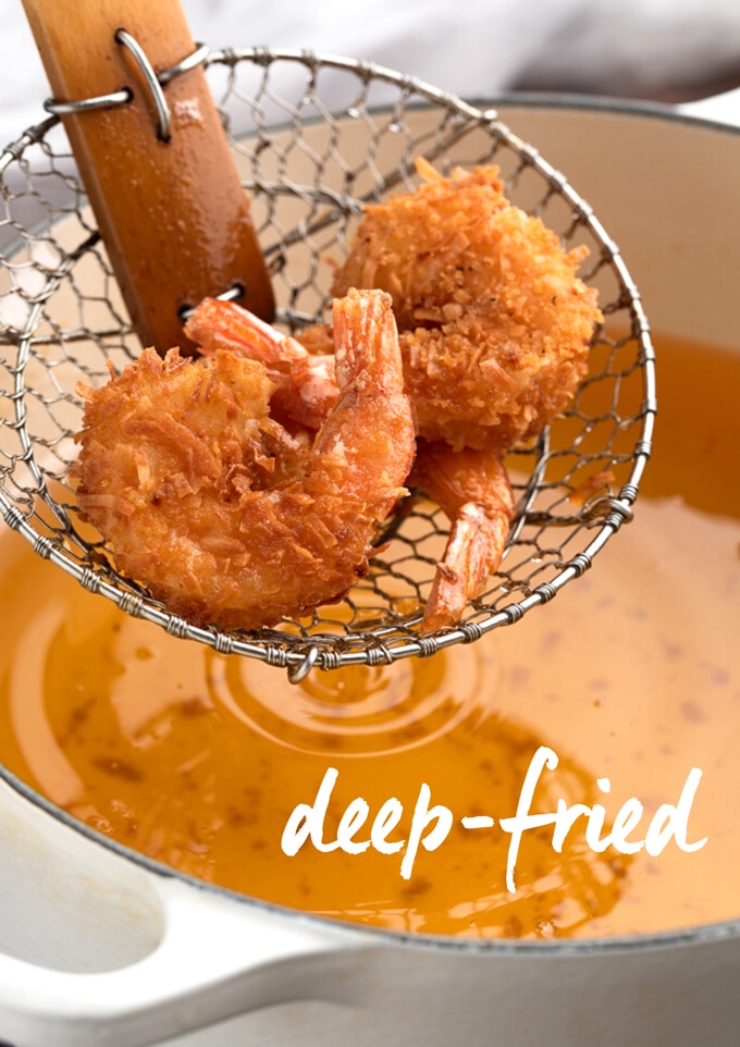 deep-fried coconut shrimp in a spider strainer over a pot of hot oil