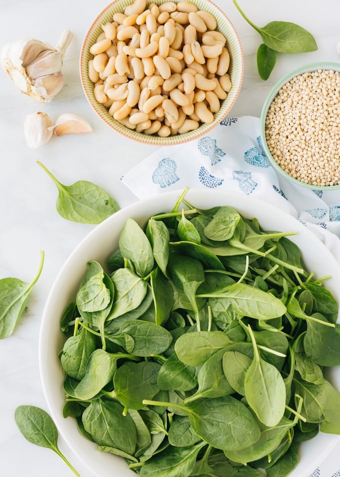 overhead view of bowls of baby spinach, cannellini beans, and dried Israeli couscous