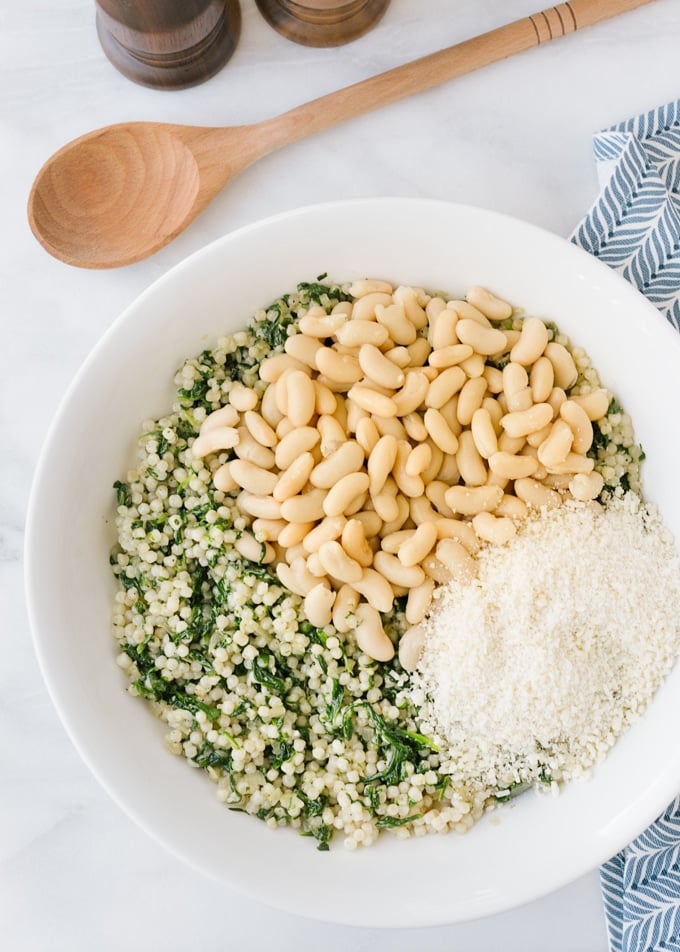 mixing pearled couscous in a white bowl with sauteed spinach, cannellini beans, and parmesan cheese