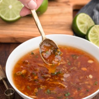 gold spoon scooping orange dipping sauce out of a white bowl