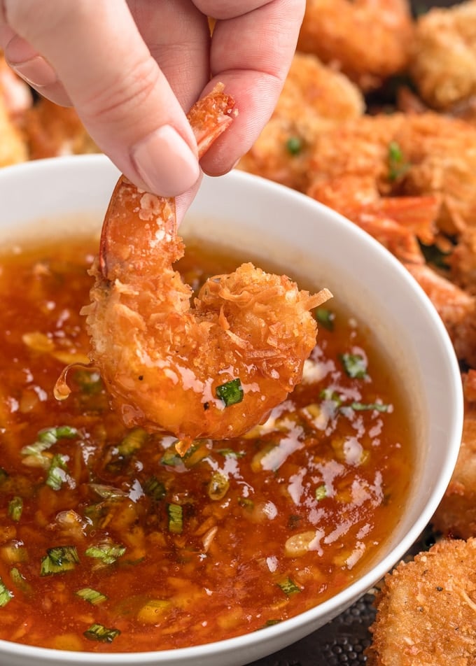 dipping a coconut shrimp into spicy orange dipping sauce in a white bowl