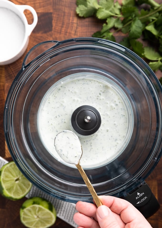 spoonful of cilantro lime sauce held over the bowl of a food processor