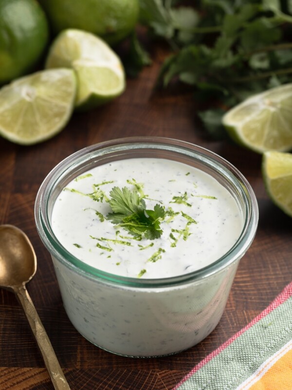 cilantro lime sauce in a glass jar on a wood board, with bunches of fresh cilantro and fresh limes