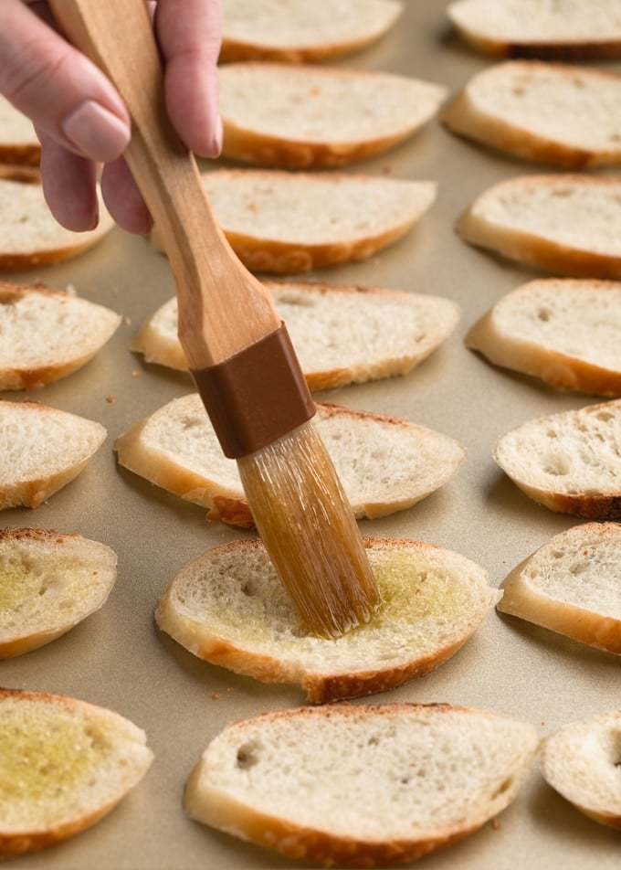 pastry brush with olive oil on sliced baguette