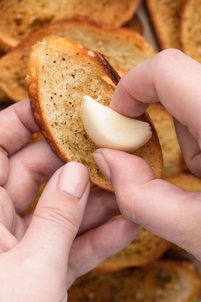 rubbing a toasted baguette slice with a clove of garlic