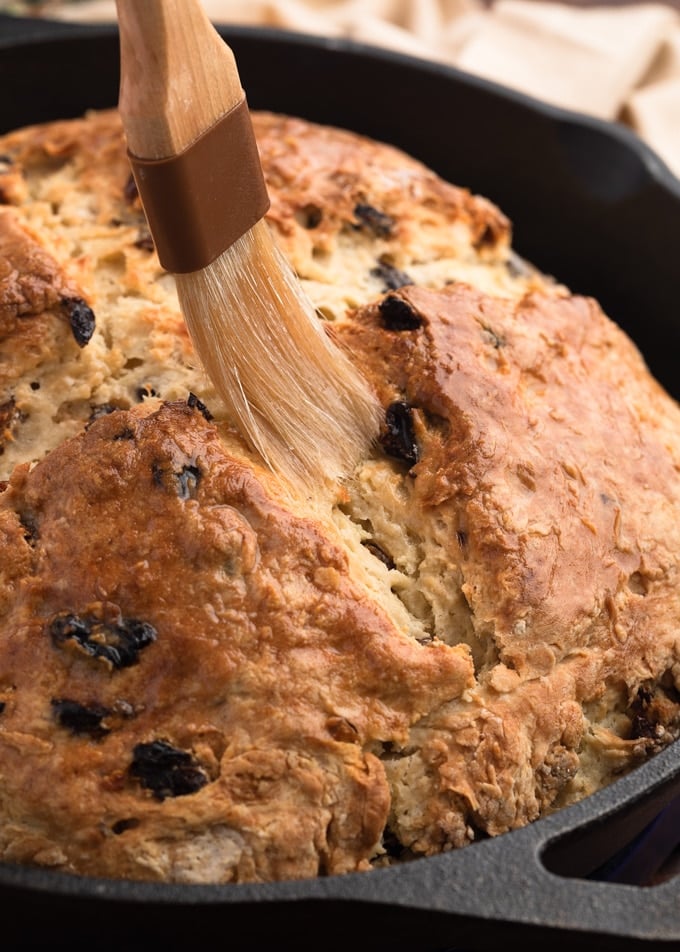 brushing melted butter onto baked soda bread in a cast iron skillet