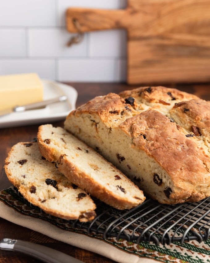 sliced loaf of American-style Irish Soda bread with raisins on a wire cooling rack, with a block of Irish butter in the background
