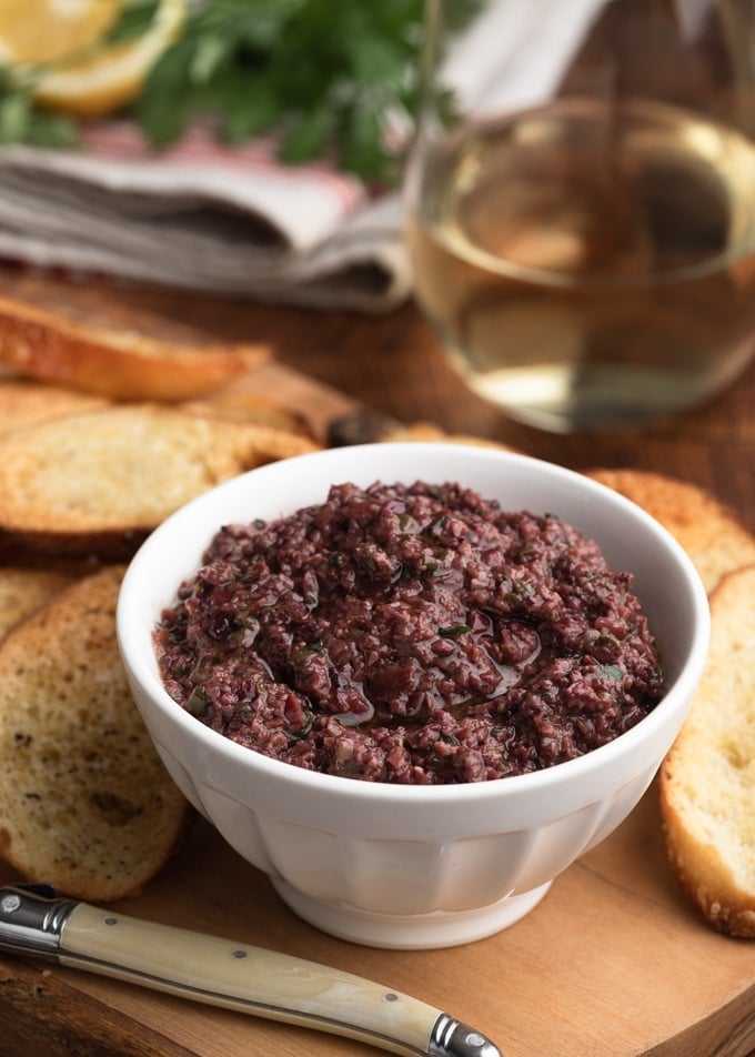 black olive tapenade in a white bowl on a serving board with crostini