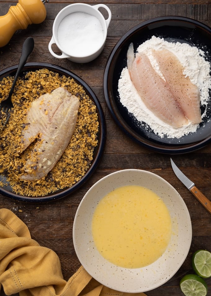 overhead photo showing tilapia fillets being breaded with flour and crushed tortilla chips