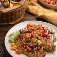 fried tortilla chip crusted tilapia fillets on an ivory plate with cherry tomato pico de gallo