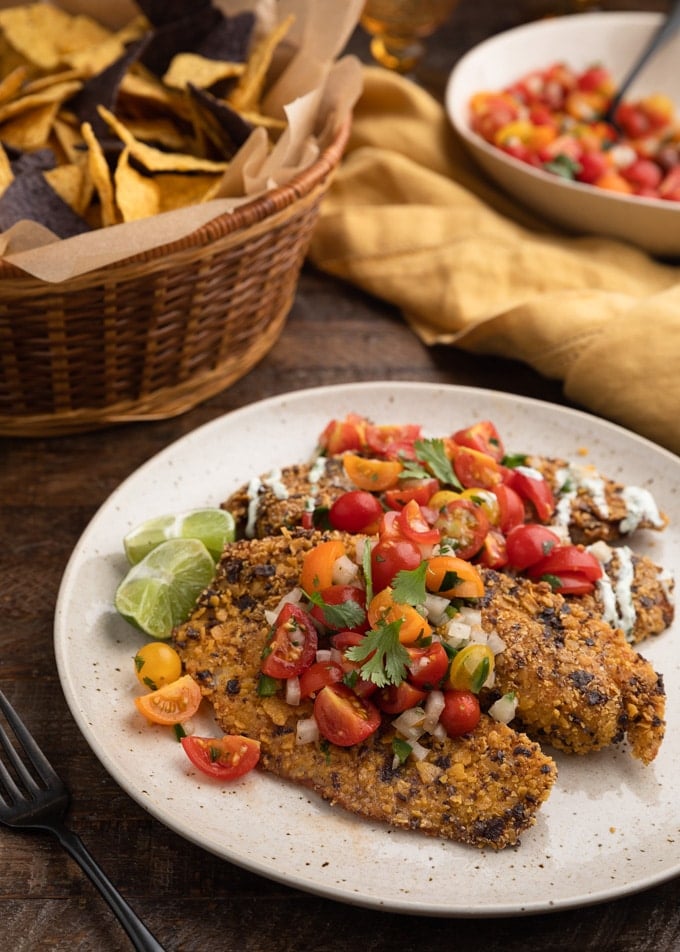 fried tortilla chip crusted tilapia fillets on an ivory plate with cherry tomato pico de gallo