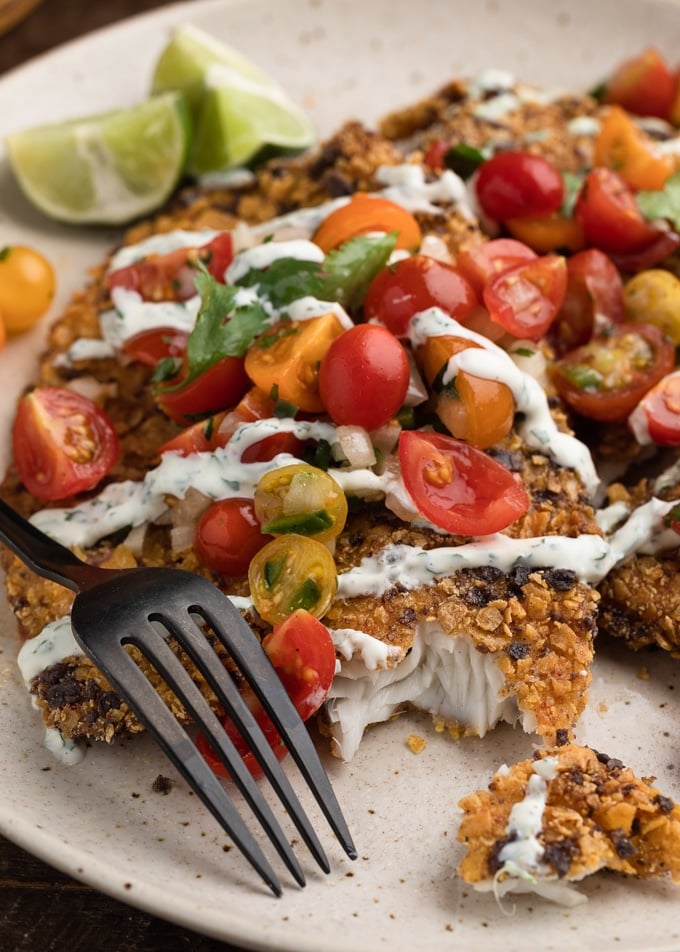 closeup of tortilla crusted tilapia with cherry tomato pico de galllo and cilantro lime sauce on a plate.