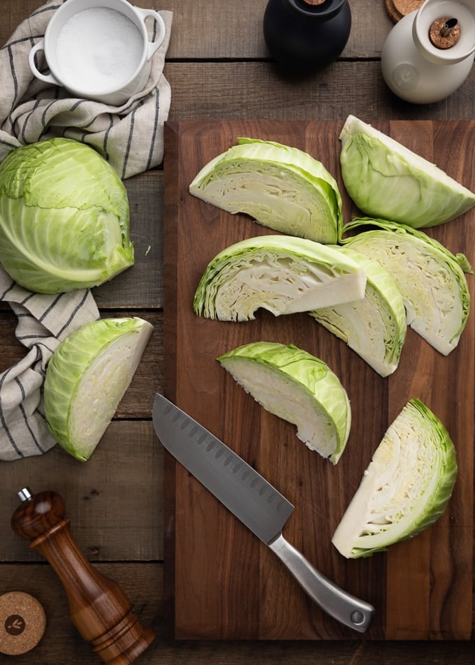 green cabbage wedges on a wood cutting board with a santoku knife