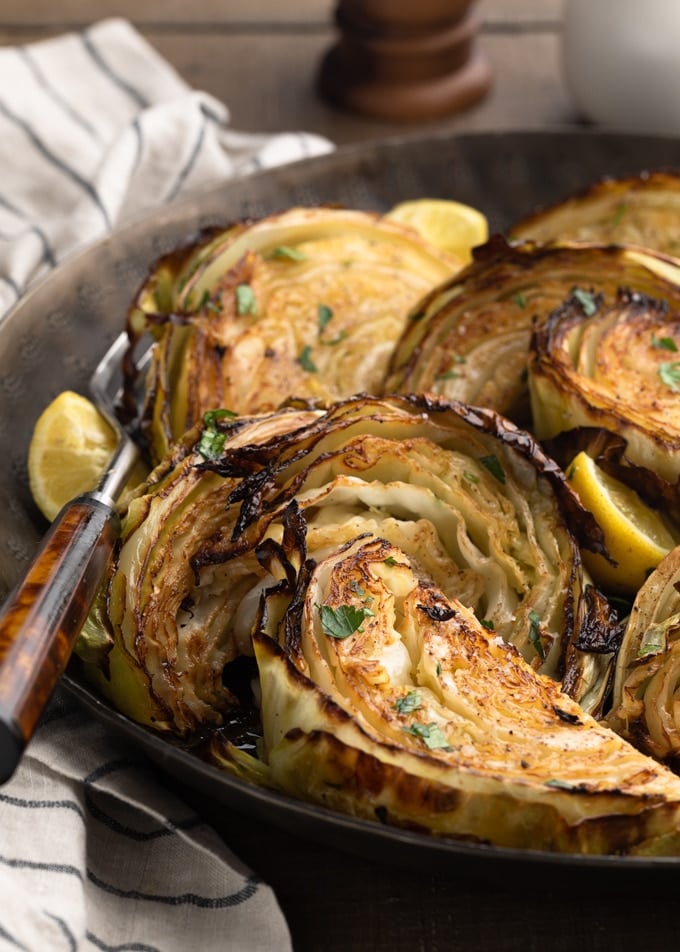 closeup of roasted cabbage wedges in a serving bowl with lemons and chopped parsley