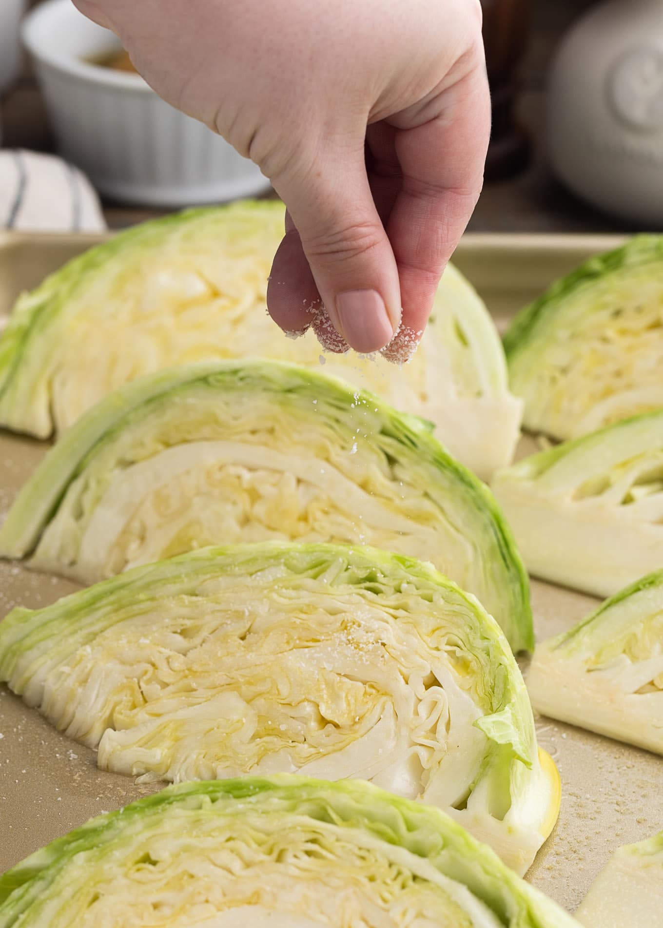 sprinkling kosher salt onto cabbage wedges on a roasting pan