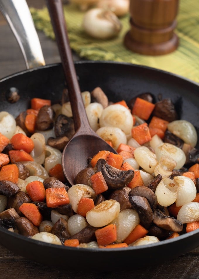 carrots, cremini mushrooms, and cippolini onions in a saute pan with a wooden spoon