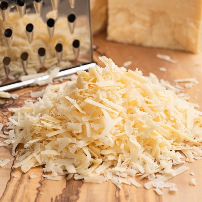shredded Irish Dubliner cheese on a wood board with a cheese grater