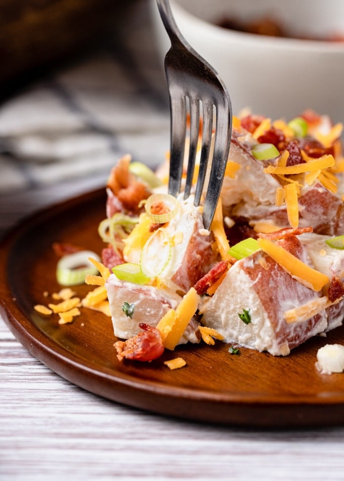 closeup side view of a fork picking up a wedge of potato salad on a wooden plate