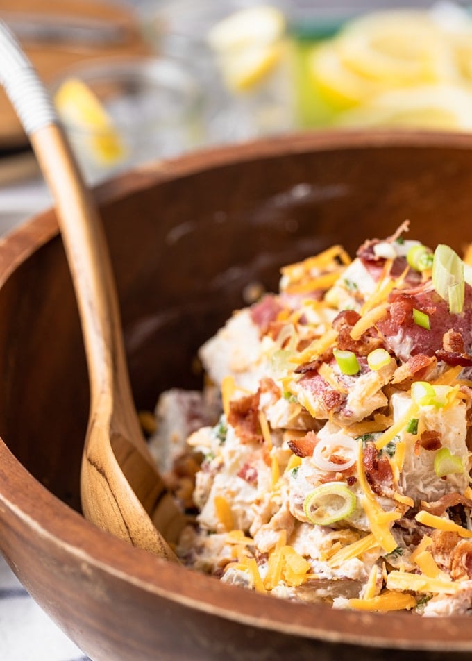 side view of loaded potato salad in a wooden bowl with a wooden serving spoon