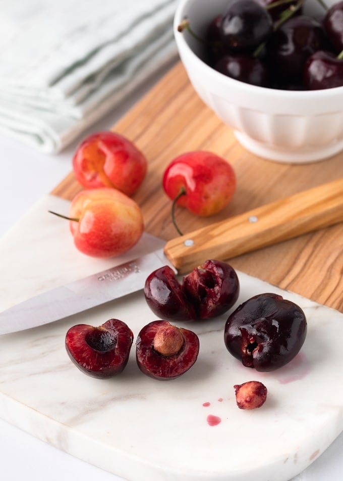 Bing cherries on a marble cutting board with a paring knife showing three cutting techniques for cherry pitting.