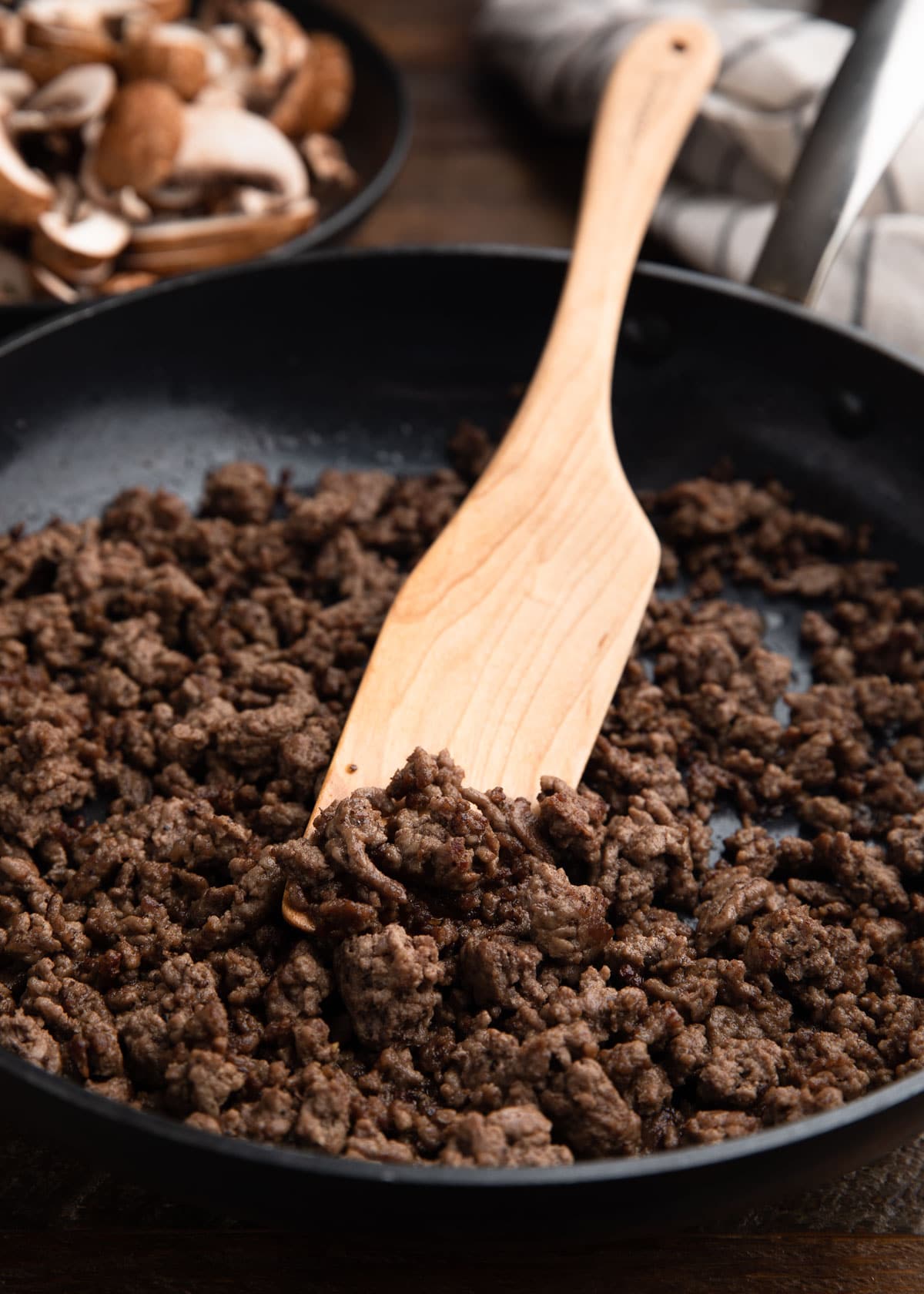 sautéed ground beef in a skillet with a wooden paddle