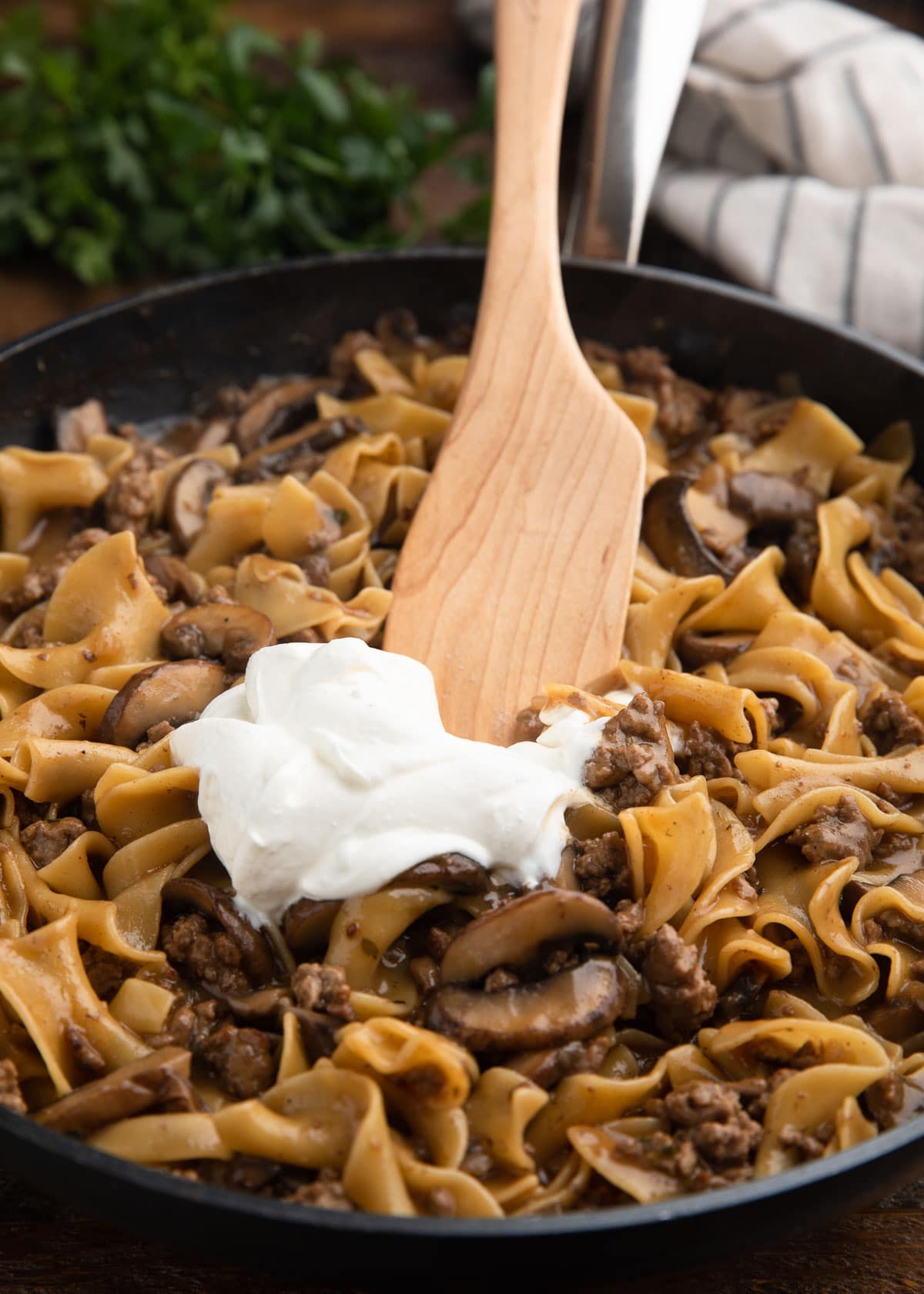 stirring sour cream into ground beef stroganoff with a wooden spoon