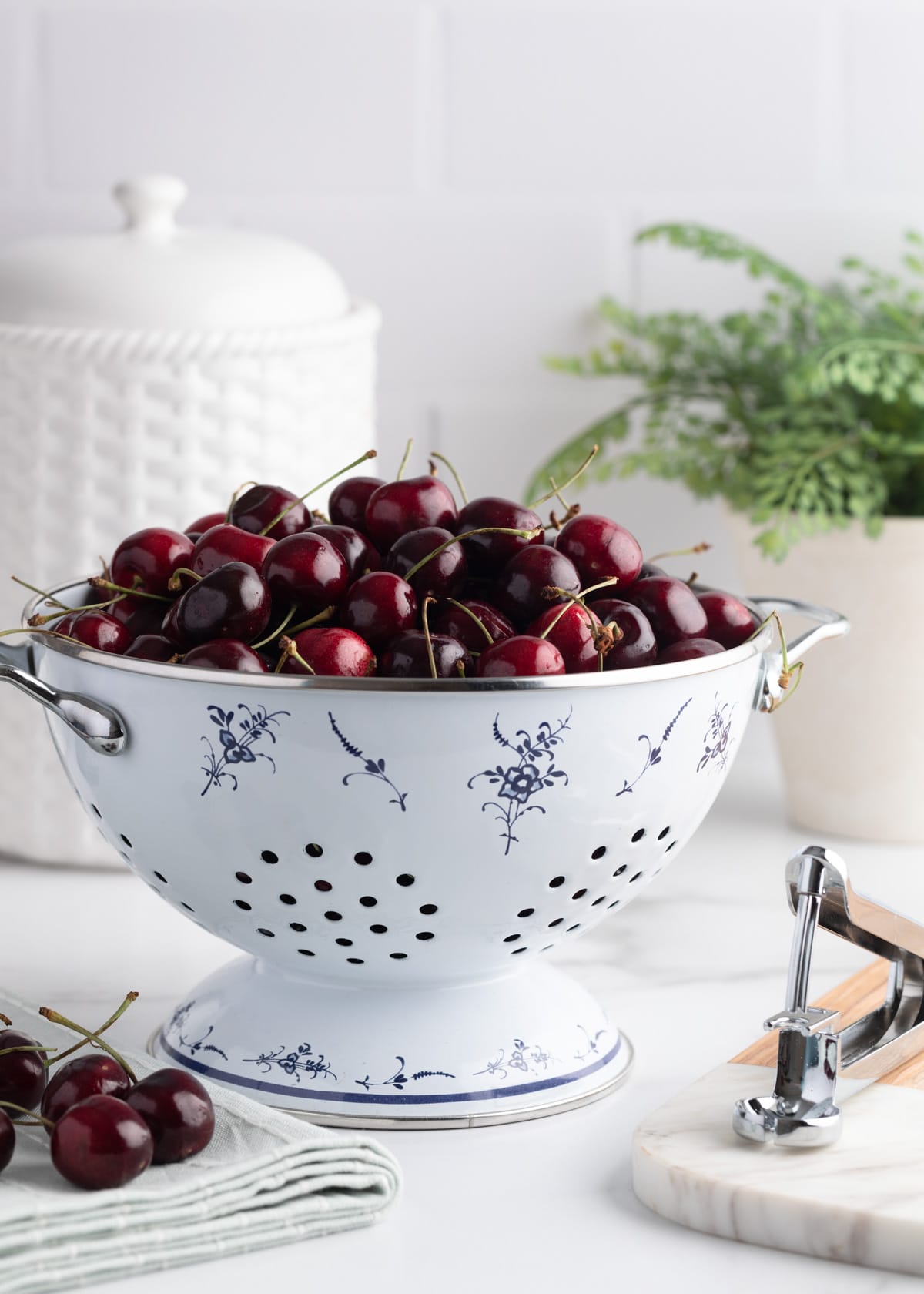 fresh bing cherries in a white enameled colander, on a marble countertop against a white subway tile kitchen background