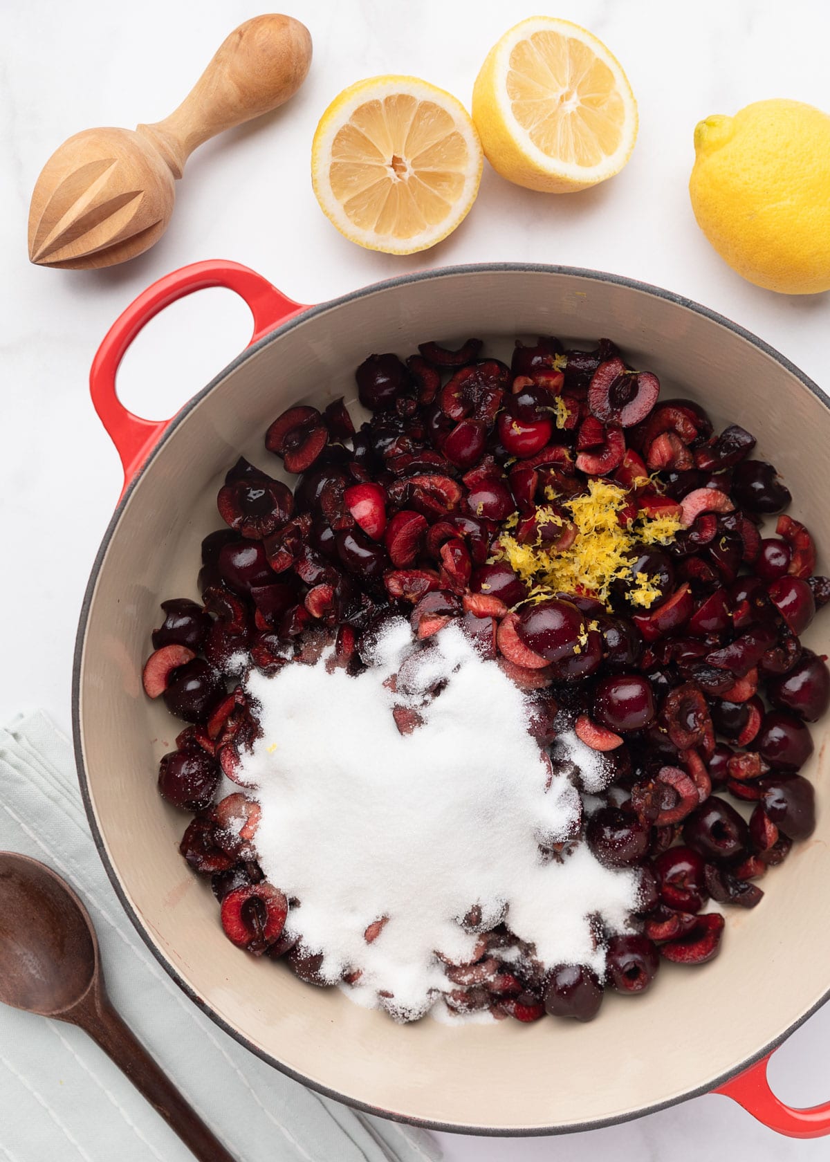 chopped cherries in an enameled cast iron pot with sugar, lemon juice, and lemon zest