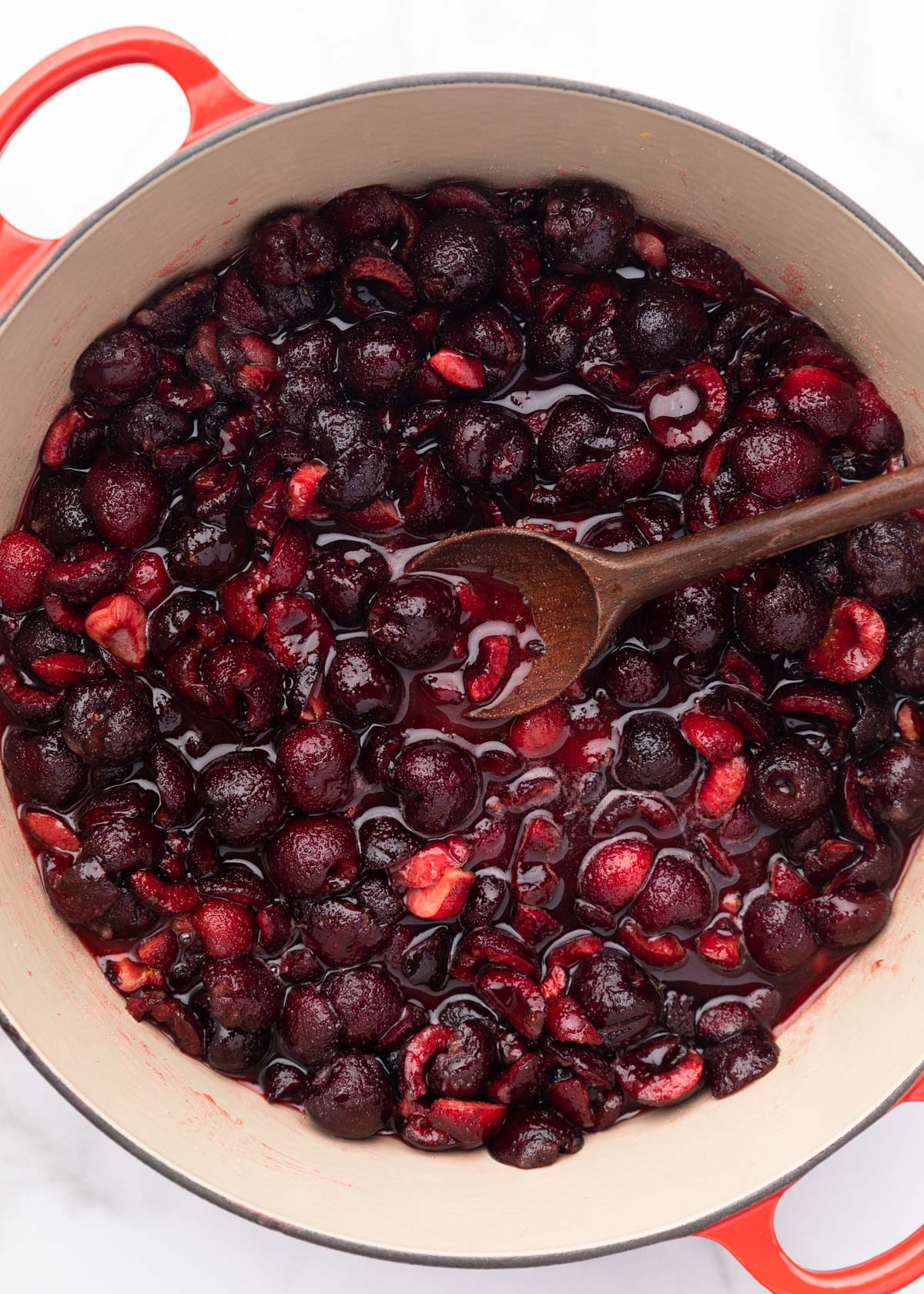 macerated Bing cherries in an enameled cast iron pot with a wooden spoon