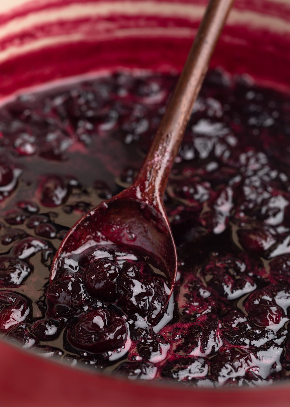 cooked cherry preserves in a pot on a wooden spoon