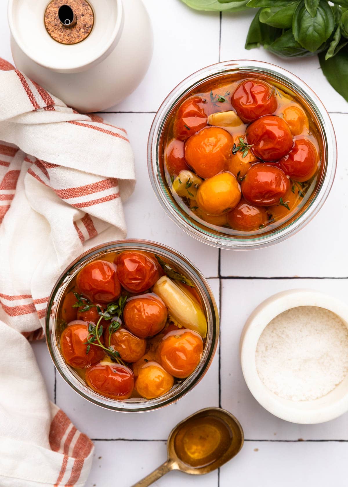 overhead of two jars of cherry tomato confit on a white tile board