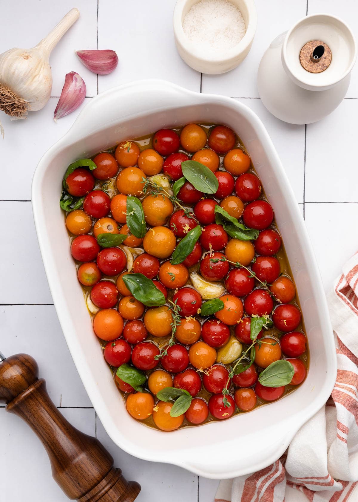 overhead of cherry tomatoes in a white ceramic baking dish with fresh herbs