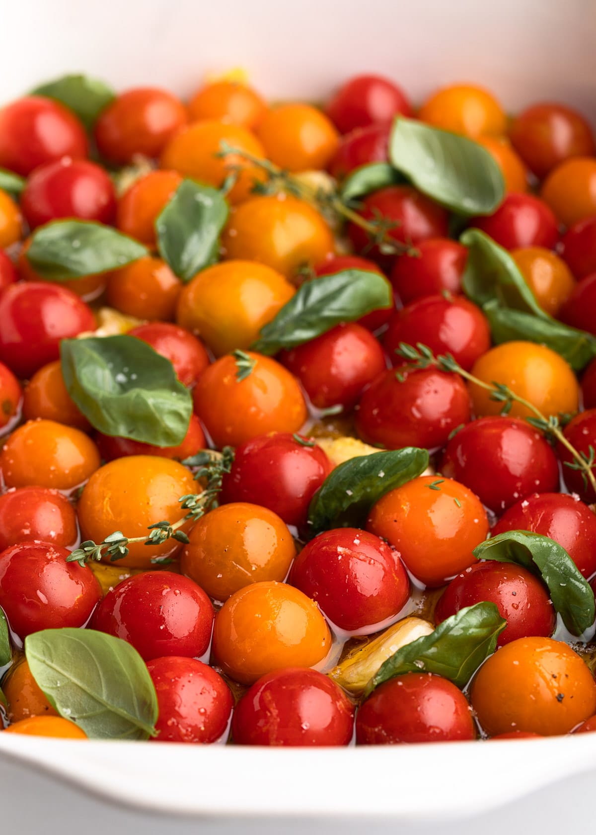 cherry tomatoes in a white ceramic baking dish with olive oil, garlic, and fresh herbs