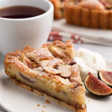 slice of fig and almond cream tart on a white plate with honey whipped cream and fresh sliced figs