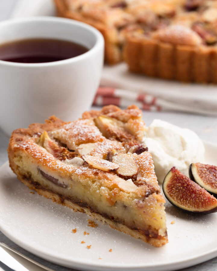 slice of fig and almond cream tart on a white plate with honey whipped cream and fresh sliced figs