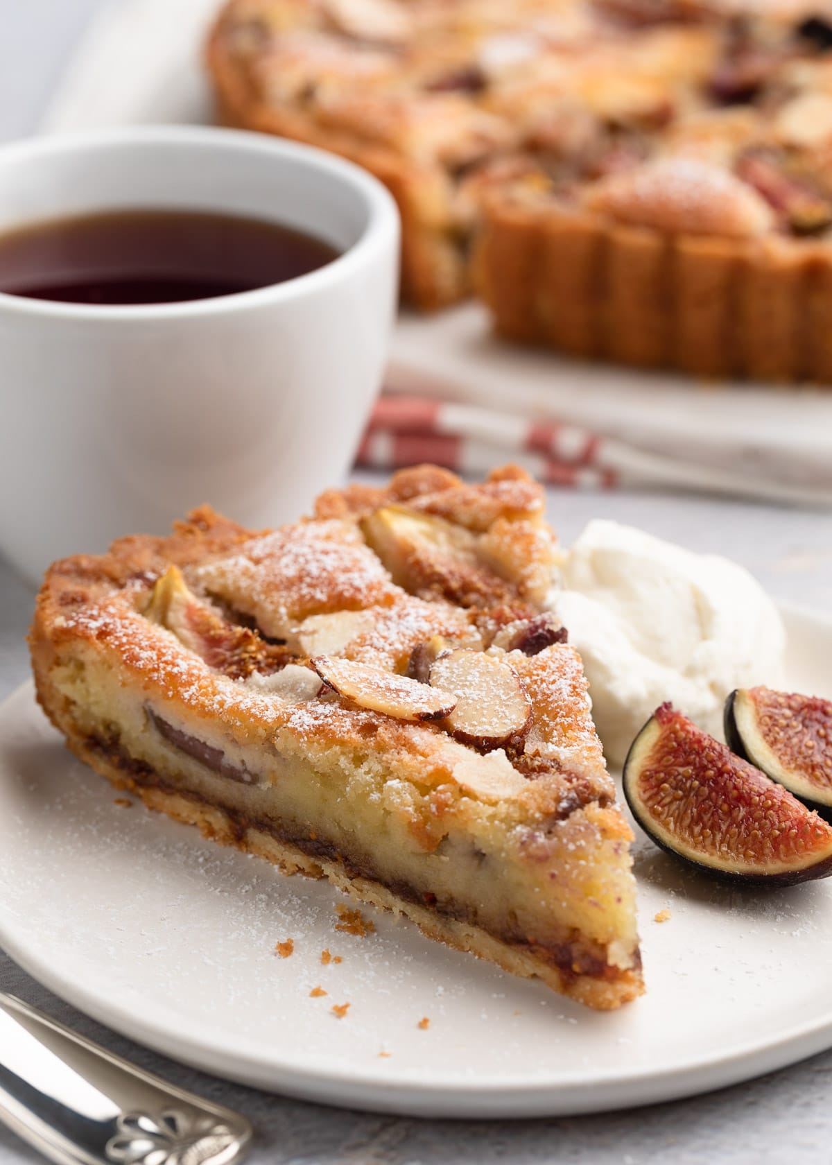 slice of fig and almond cream tart on a white plate with honey whipped cream and fresh sliced figs