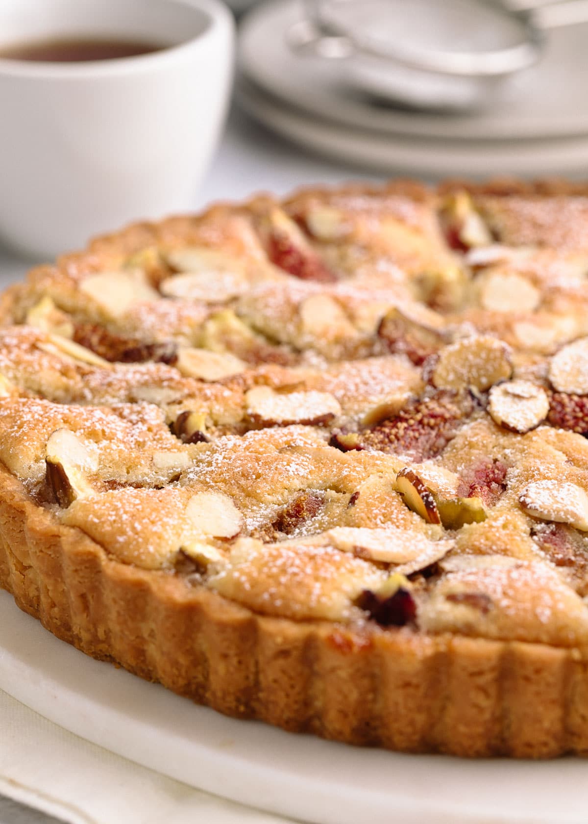 side view of a baked fig and almond cream tart on a white marble board