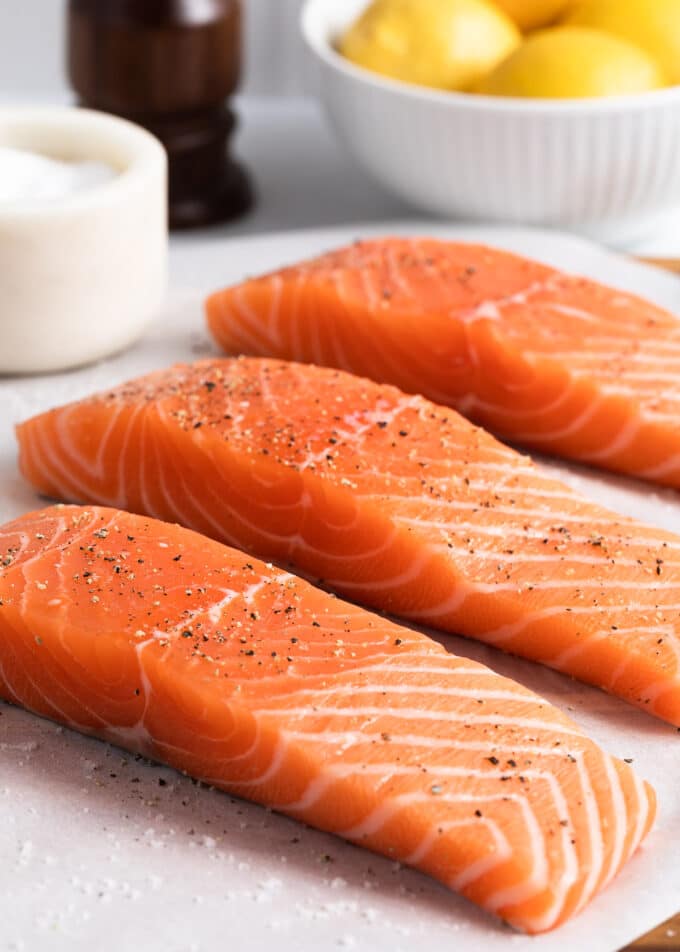 three raw salmon fillets on parchment paper seasoned with salt and pepper