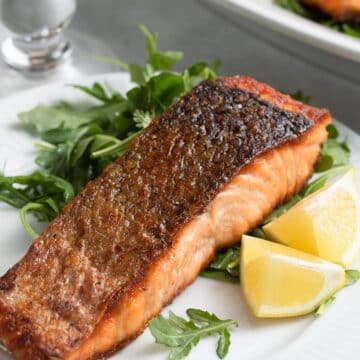 pan seared salmon on a white plate with arugula salad and lemon wedges