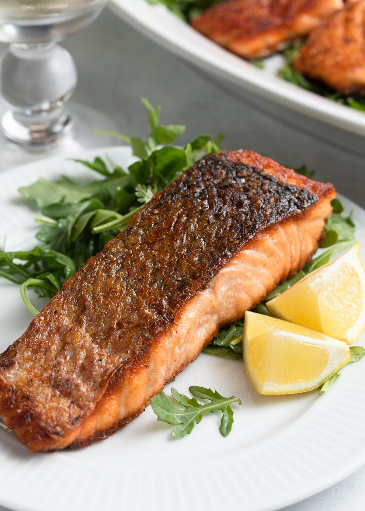 pan seared salmon on a white plate with arugula salad and lemon wedges